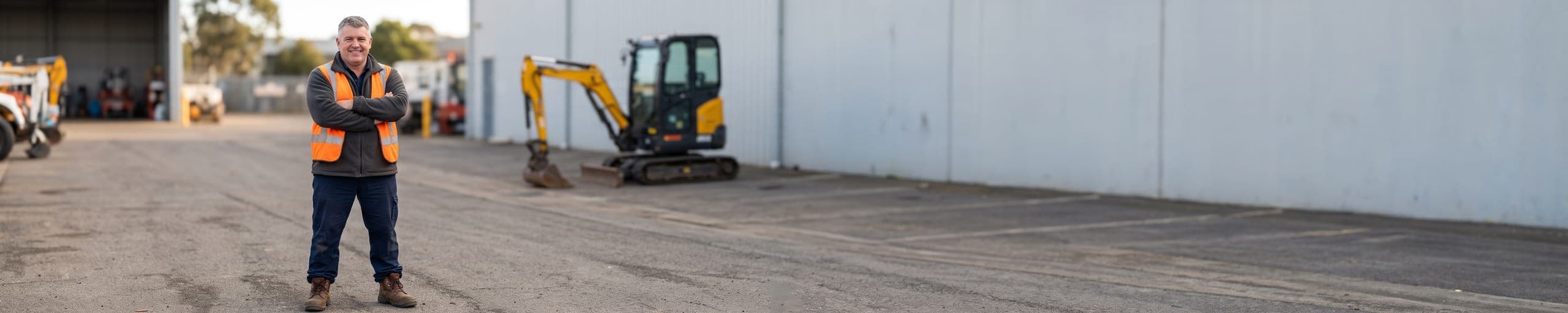 Loueur guidant par gestes le chargement d'un bulldozer sur une remorque surbaissée, autres engins de terrassement visibles dans le parc de location à l'arrière-plan